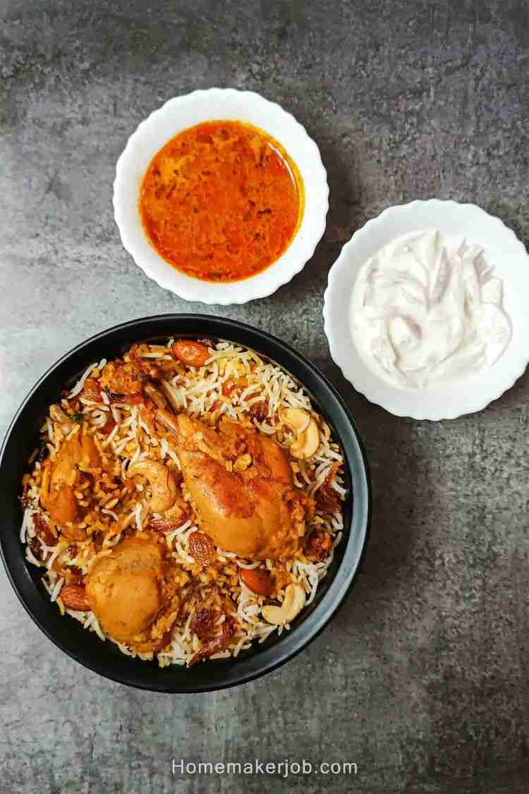 Top view photo of mughlai biryani in a black bowl, along with raita and curry in white bowls on a table, a recipe by homemakerjob.com